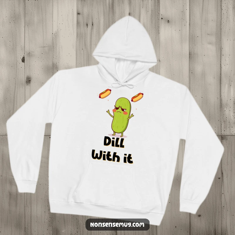 Funny hoodie showing a grumpy pickle looking confused while expertly juggling three flying hot dogs with comedic flair.